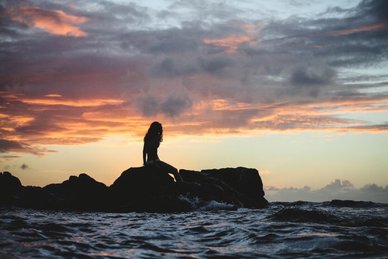 A Mermaid Sitting on a rock under a sunset