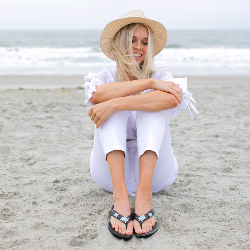 smiling woman sitting on the beach in cute beach sandals