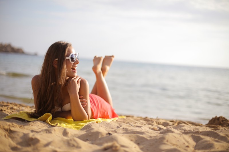 woman wearing sunglasses while lying on beach sand